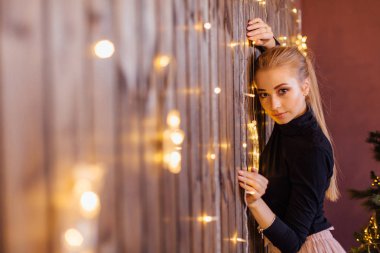 Yıldız ve ay ışıkları ile ahşap duvarın yanında duran bir kazak ve etek giymiş güzel genç kadın