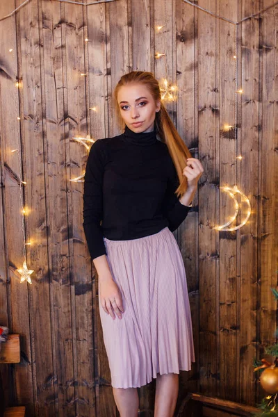 Bella giovane donna vestita con un maglione e gonna in piedi accanto al muro di legno con stelle e luci lunari — Foto Stock