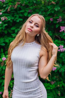 Leylak çalıyanında duran güzel beyaz elbise giyen büyüleyici sarışın bir kadın portresi.