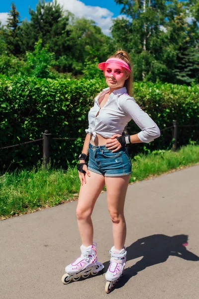 Retrato de una chica emocional en una visera de gorra rosa y guantes protectores para patines y patinetas montadas en patines en la carretera . — Foto de Stock