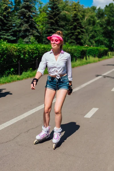 Portrait of an emotional girl in a pink cap visor and protective gloves for rollerblades and skateboarding riding on rollerblades on the road. — Stock Photo, Image