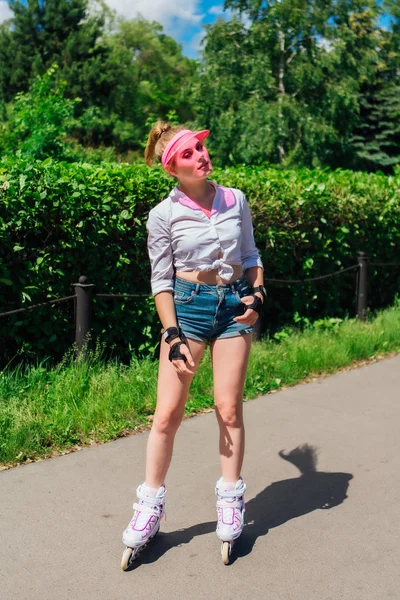 Portrait of an emotional girl in a pink cap visor and protective gloves for rollerblades and skateboarding riding on rollerblades on the road. — Stock Photo, Image