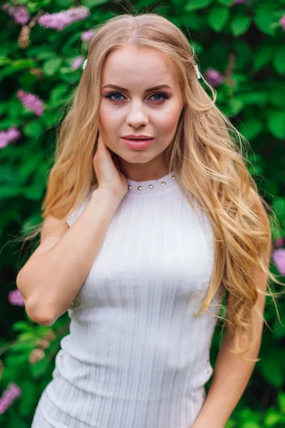 Retrato de una encantadora mujer rubia con hermoso vestido blanco de pie junto al arbusto lila . —  Fotos de Stock