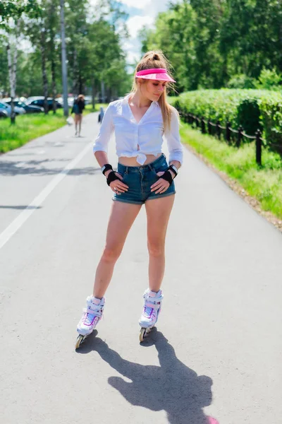 Retrato de una chica emocional en una visera de gorra rosa y guantes protectores para patines y patinetas montadas en patines en la carretera . —  Fotos de Stock