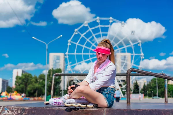 Retrato de una chica emocional en una visera de gorra rosa con guantes protectores y patines sentados en el fondo de la rueda de los hurones . — Foto de Stock