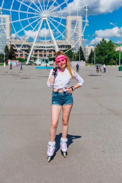 Retrato de una chica emocional en una visera de gorra rosa y guantes protectores para patines y patinetas montadas en patines en la carretera . — Foto de Stock