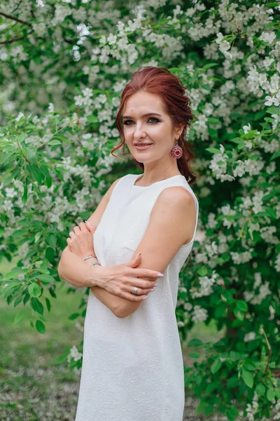 Mujer encantadora vistiendo hermoso vestido blanco de pie bajo el manzano — Foto de Stock