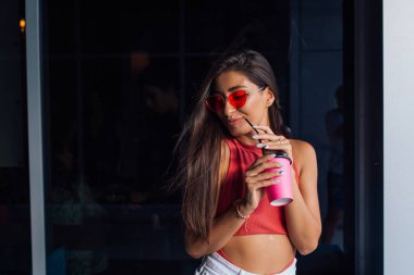 Şık mutlu genç esmer kadın gitmek için kahve pembe fincan tutan.