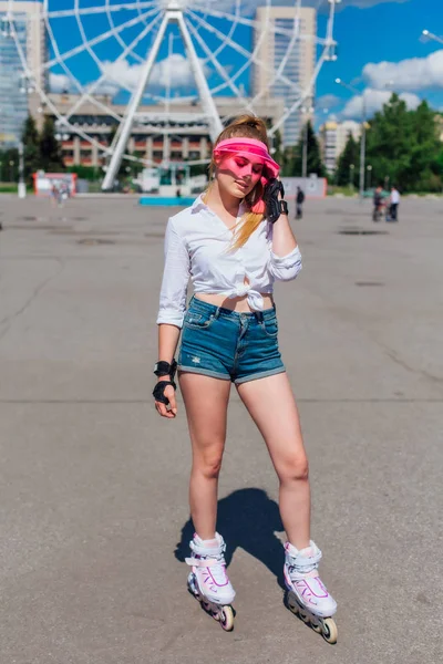 Retrato de una chica emocional en una visera de gorra rosa y guantes protectores para patines y patinetas montadas en patines en la carretera . — Foto de Stock