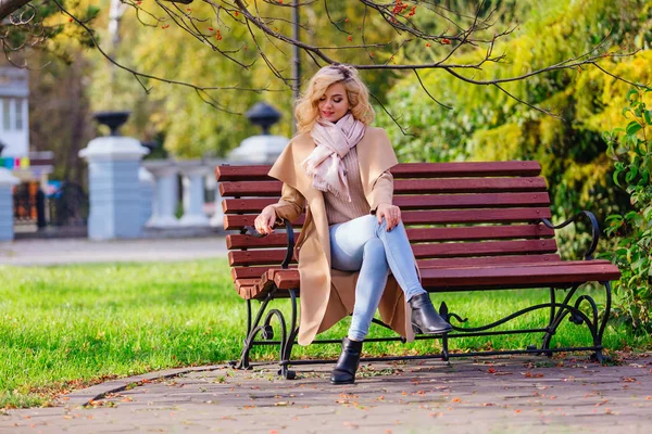 Jonge mooie vrouw zittend op de Bank in herfst Park — Stockfoto