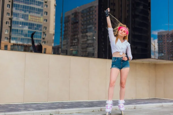 Potret seorang gadis emosional dalam topi merah muda dan sarung tangan pelindung untuk rollerblades dan skateboarding naik rollerblades di jalan . — Stok Foto