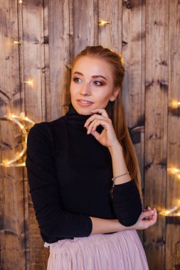 Yıldız ve ay ışıkları ile ahşap duvarın yanında duran bir kazak ve etek giymiş güzel genç kadın