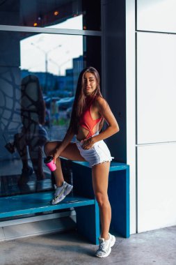 Beyaz şort ve spor ayakkabı giyen şık mutlu genç esmer kadın gitmek için kahve pembe fincan tutan.