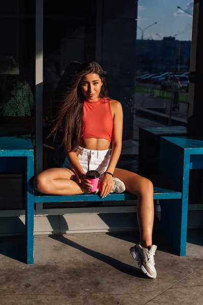 Élégante jeune femme brune heureuse portant un short blanc et des baskets tenant une tasse de café rose à emporter . — Photo