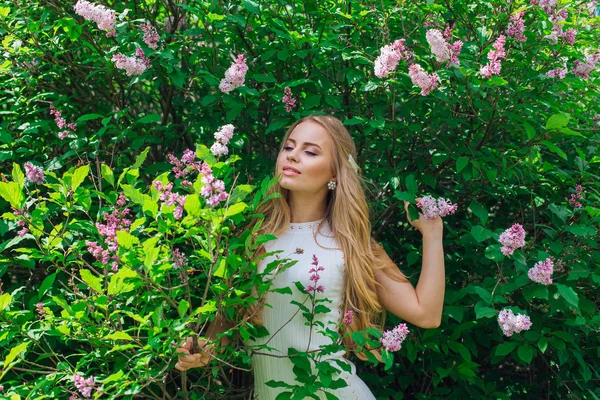 Leylak çalıyanında duran güzel beyaz elbise giyen büyüleyici sarışın bir kadın portresi.