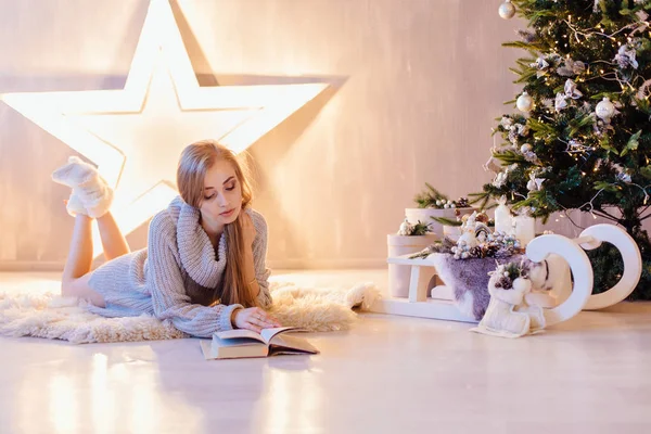 Piękna młoda kobieta, układanie i czytanie książki pod choinkę w wakacje wnętrze — Zdjęcie stockowe