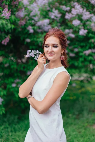 Encantadora mujer con hermoso vestido blanco de pie junto al arbusto lila — Foto de Stock