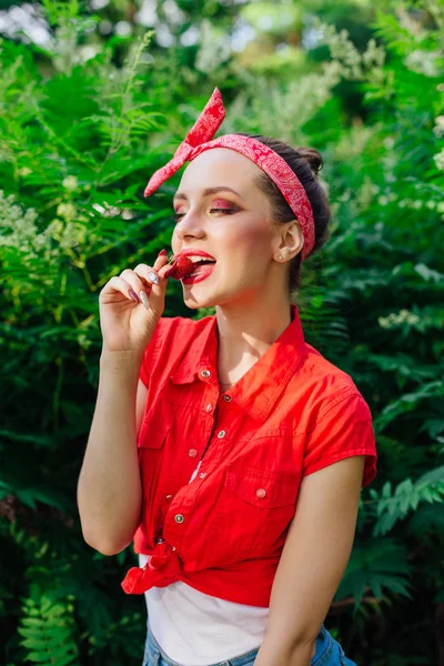 Mooie jonge pin-up meisje met heldere make-up eten van verse natuurlijke aardbei. — Stockfoto