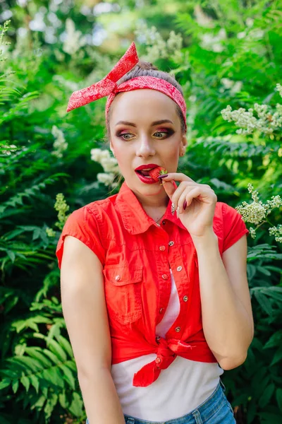 Mooie jonge pin-up meisje met heldere make-up eten van verse natuurlijke aardbei. — Stockfoto