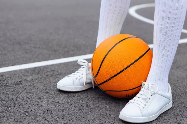De cerca los pies de wonan en zapatillas blancas y calcetines largos whote, con una pelota en una cancha de baloncesto . — Foto de Stock