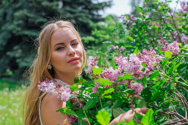 Retrato de una encantadora mujer rubia con hermoso vestido blanco de pie junto al arbusto lila . —  Fotos de Stock