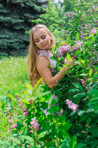 Leylak çalıyanında duran güzel beyaz elbise giyen büyüleyici sarışın bir kadın portresi.