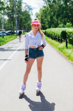 Pembe bir kapak Visor ve paten için koruyucu eldivenler ve yolda paten üzerinde kaykay sürme duygusal bir kız portresi.