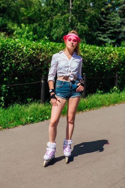 Portrait of an emotional girl in a pink cap visor and protective gloves for rollerblades and skateboarding riding on rollerblades on the road. — Stock Photo, Image