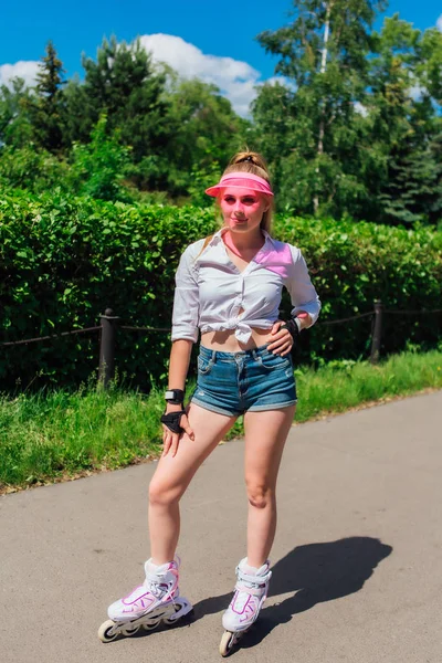 Retrato de una chica emocional en una visera de gorra rosa y guantes protectores para patines y patinetas montadas en patines en la carretera . —  Fotos de Stock