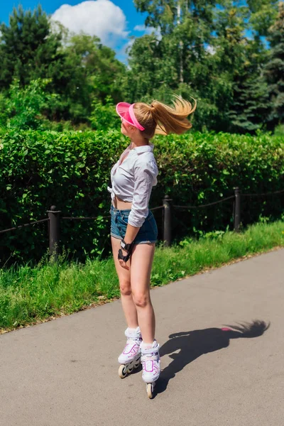 Portrait of an emotional girl in a pink cap visor and protective gloves for rollerblades and skateboarding riding on rollerblades on the road. — Stock Photo, Image