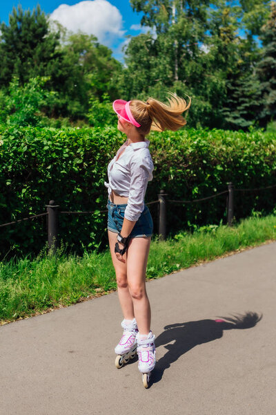 Portrait of an emotional girl in a pink cap visor and protective gloves for rollerblades and skateboarding riding on rollerblades on the road.