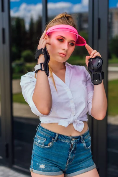 Porträtt av en känslomässig flicka i en rosa mössa visir och skyddshandskar för rullskridskor och skateboard. — Stockfoto