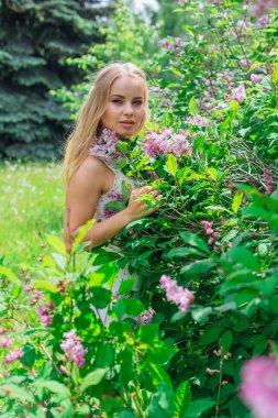 Leylak çalıyanında duran güzel beyaz elbise giyen büyüleyici sarışın bir kadın portresi.