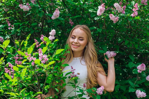 Leylak çalıyanında duran güzel beyaz elbise giyen büyüleyici sarışın bir kadın portresi.