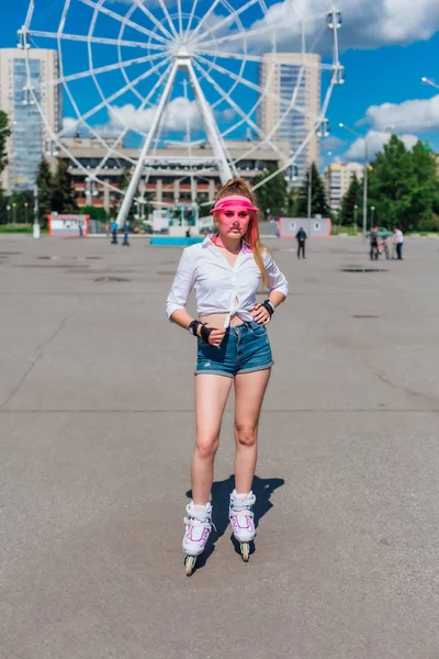 Porträtt av en känslomässig flicka i en rosa mössa visir och skyddshandskar för rullskridskor och skateboard ridning på rullskridskor på vägen. — Stockfoto