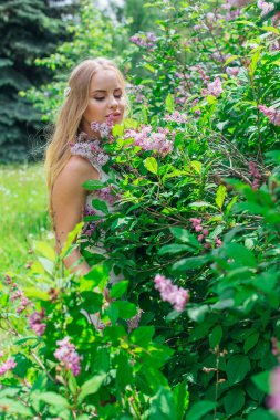 Leylak çalıyanında duran güzel beyaz elbise giyen büyüleyici sarışın bir kadın portresi.