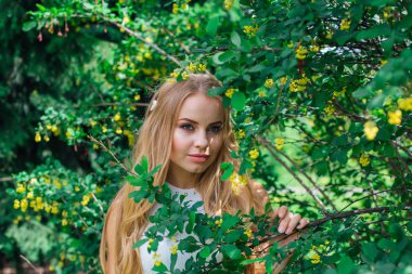 Barberry çalı yanında duran güzel beyaz elbise giyen büyüleyici bir sarışın kadının portresi kadar yakın.