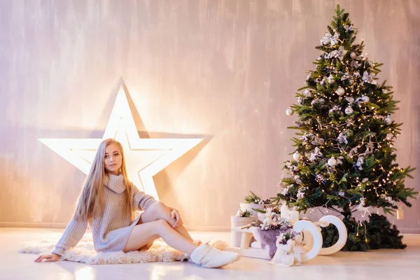 Hermosa joven posando bajo el árbol de Navidad en un interior de vacaciones —  Fotos de Stock