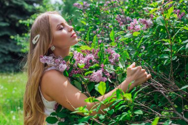 Leylak çalıyanında duran güzel beyaz elbise giyen büyüleyici sarışın bir kadın portresi.