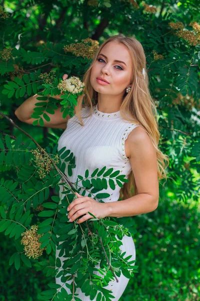 Retrato de una encantadora mujer rubia con hermoso vestido blanco de pie junto al rowan tree . — Foto de Stock