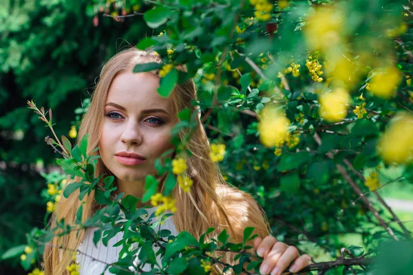 Närbild porträtt av en charmig blond kvinna klädd i vacker vit klänning står bredvid Berberis buske. — Stockfoto