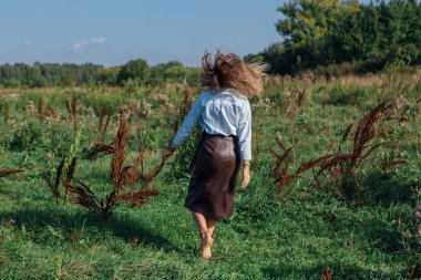 Yeşil bir tarlada yürüyen mutlu genç ve güzel bir kadın