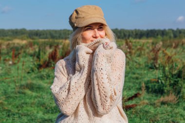 Yeşil bir tarlada yürüyen mutlu, güzel sarışın kadın.