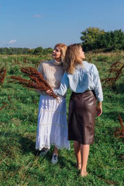 Yazın sonlarında bir tarlada iki güzel kadının portresi. Güzel kızlar yan yana durur ve kuru kahverengi bitkilerden buket tutarlar..