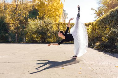 Sonbahar parkında beyaz etekli kadın balerin sivri uçlu ayakkabılarla dans ediyor..
