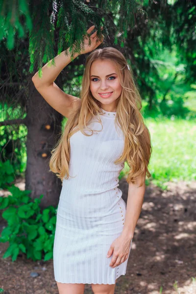 Porträt einer charmanten blonden Frau in schönem weißen Kleid, die unter einem Tannenbaum steht. — Stockfoto