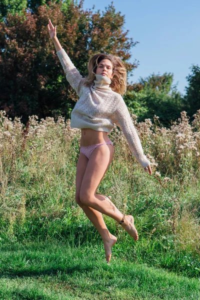 Happy young beautiful woman jumping with bare foot in a green field