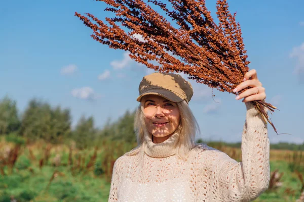 Happy beautiful blond woman walking in a green field with a bouquete of dry brown plants — Stock Photo, Image