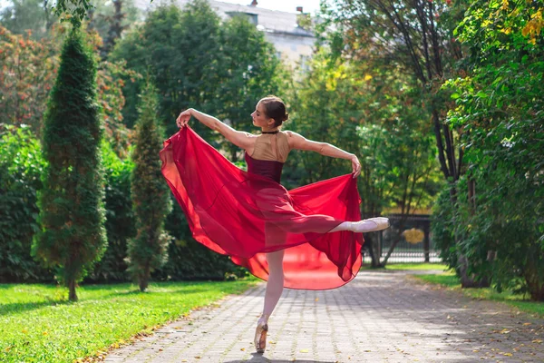 Bailarina de mujer en vestido de ballet rojo bailando en zapatos puntiagudos en el parque de otoño . —  Fotos de Stock