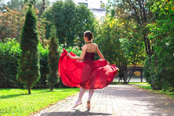 Mulher bailarina em vestido de balé vermelho dançando em sapatos pointe no parque de outono . — Fotografia de Stock